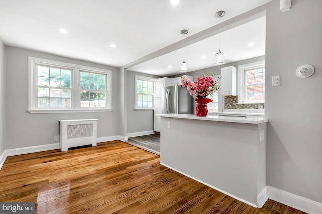 kitchen with stainless steel refrigerator, white cabinets, decorative backsplash, hanging light fixtures, and light hardwood / wood-style floors