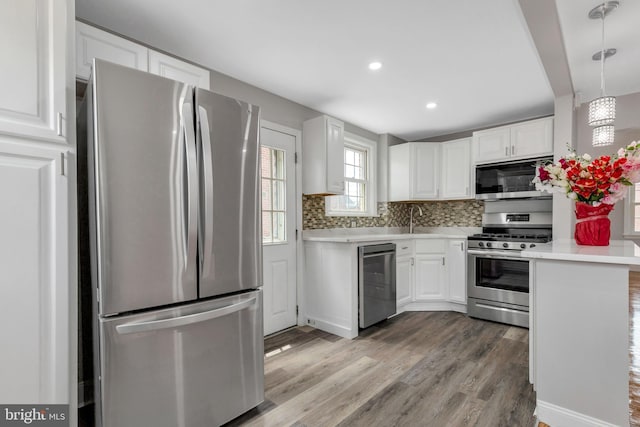 kitchen featuring pendant lighting, backsplash, white cabinetry, and stainless steel appliances