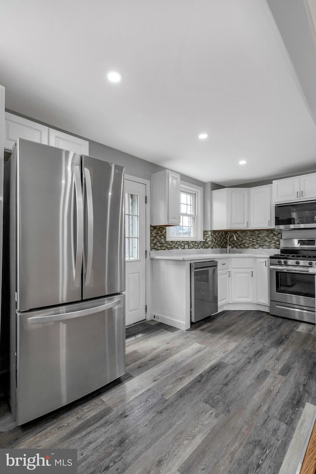 kitchen featuring stainless steel appliances, white cabinetry, dark hardwood / wood-style floors, and backsplash