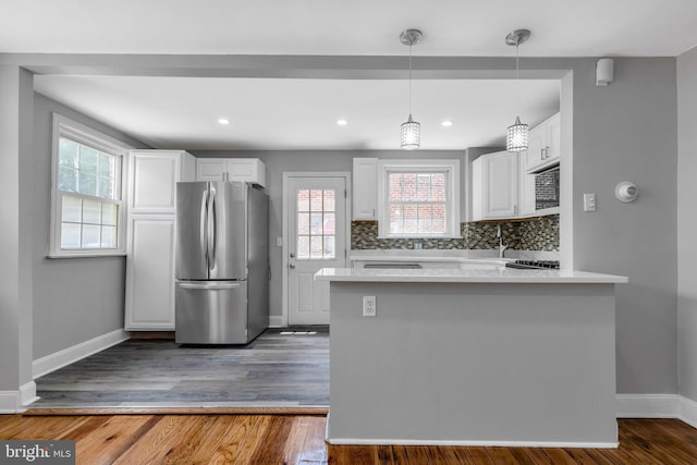 kitchen with tasteful backsplash, hanging light fixtures, stainless steel refrigerator, kitchen peninsula, and white cabinets