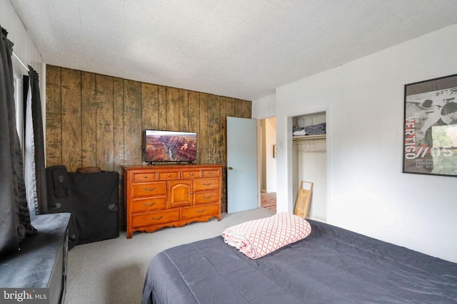 bedroom featuring a textured ceiling, a closet, wooden walls, and light carpet