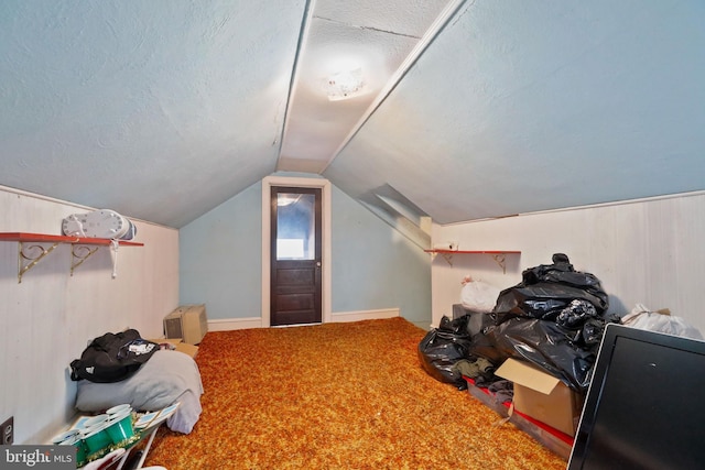 additional living space featuring a textured ceiling, lofted ceiling, wooden walls, and carpet flooring