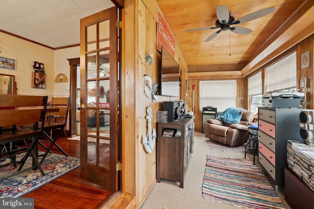 interior space with wood walls, carpet, ceiling fan, wooden ceiling, and ornamental molding