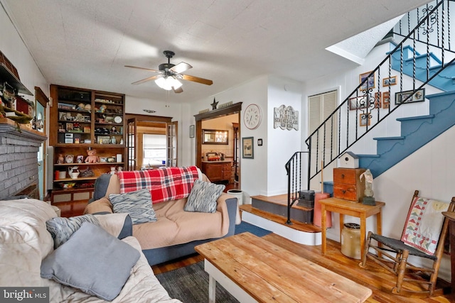 living room with a brick fireplace, ceiling fan, hardwood / wood-style flooring, and a textured ceiling