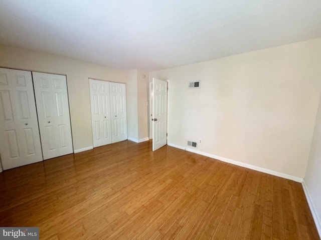 unfurnished bedroom with multiple closets and hardwood / wood-style floors