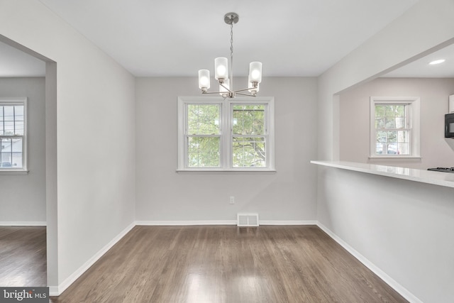 unfurnished dining area featuring an inviting chandelier, plenty of natural light, and dark wood-type flooring