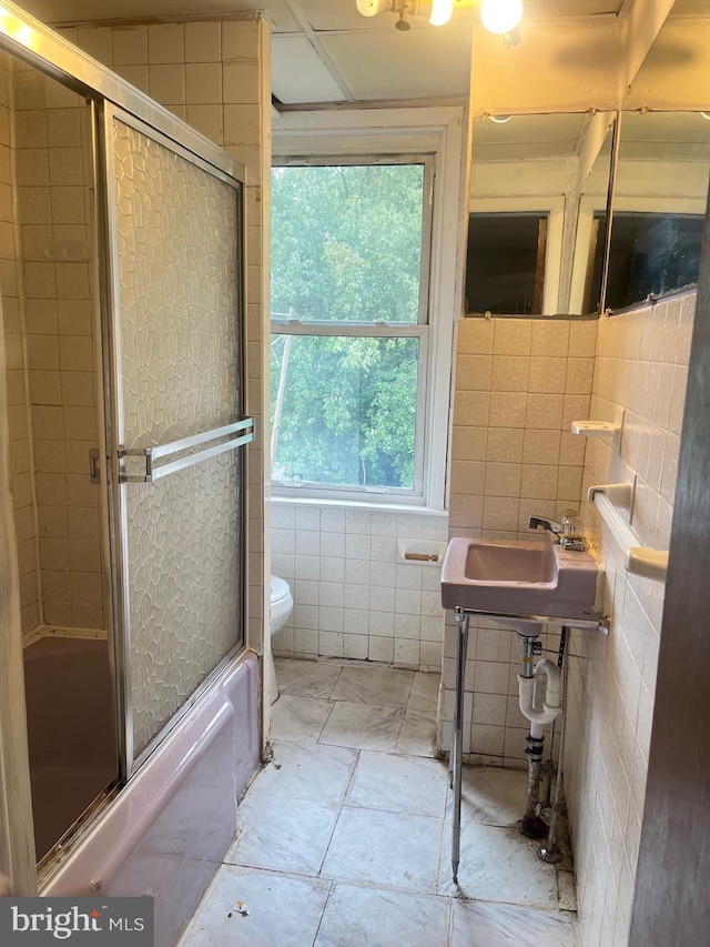 bathroom featuring bath / shower combo with glass door, tile walls, and toilet