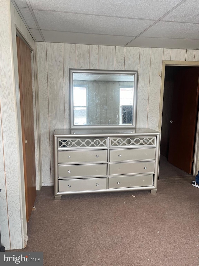 unfurnished bedroom with dark carpet, wood walls, and a paneled ceiling