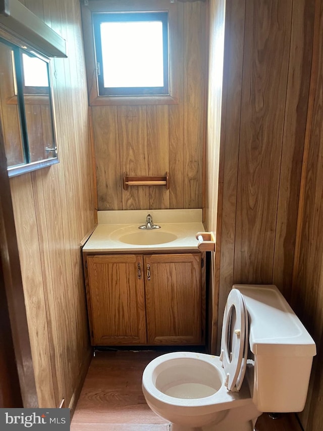 bathroom featuring wooden walls, hardwood / wood-style floors, vanity, and toilet