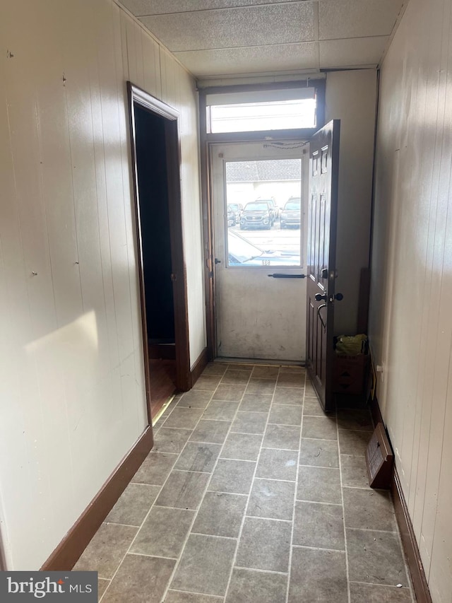 corridor with a drop ceiling, wood walls, and light tile patterned flooring