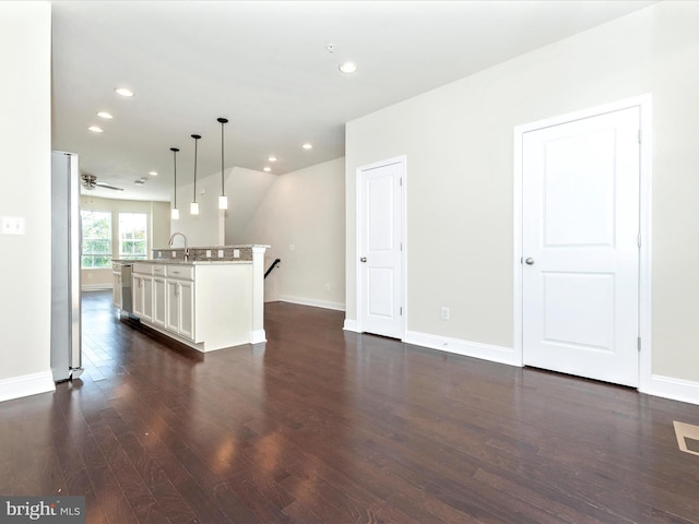 interior space with an island with sink, dark hardwood / wood-style floors, white cabinets, stainless steel fridge, and decorative light fixtures