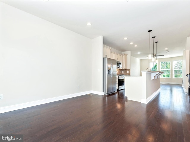 kitchen with a kitchen breakfast bar, dark wood-type flooring, a center island with sink, decorative light fixtures, and stainless steel appliances