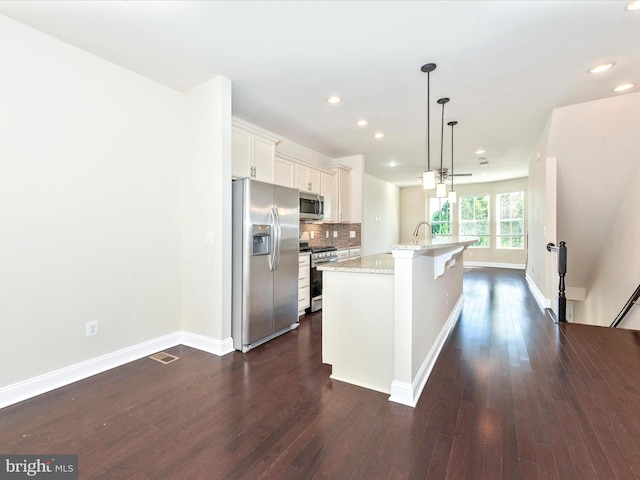 kitchen with an island with sink, hanging light fixtures, white cabinetry, appliances with stainless steel finishes, and dark hardwood / wood-style floors