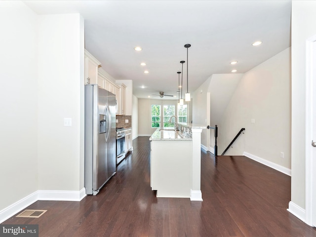 kitchen with an island with sink, light stone counters, dark hardwood / wood-style floors, appliances with stainless steel finishes, and decorative light fixtures