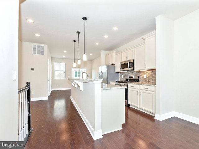 kitchen featuring a kitchen island with sink, dark hardwood / wood-style flooring, hanging light fixtures, white cabinets, and appliances with stainless steel finishes