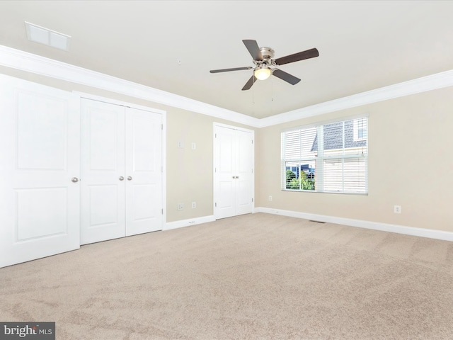 unfurnished bedroom with ornamental molding, light colored carpet, multiple closets, and ceiling fan