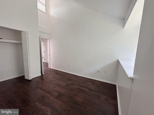 unfurnished bedroom featuring a high ceiling, a closet, and dark wood-type flooring