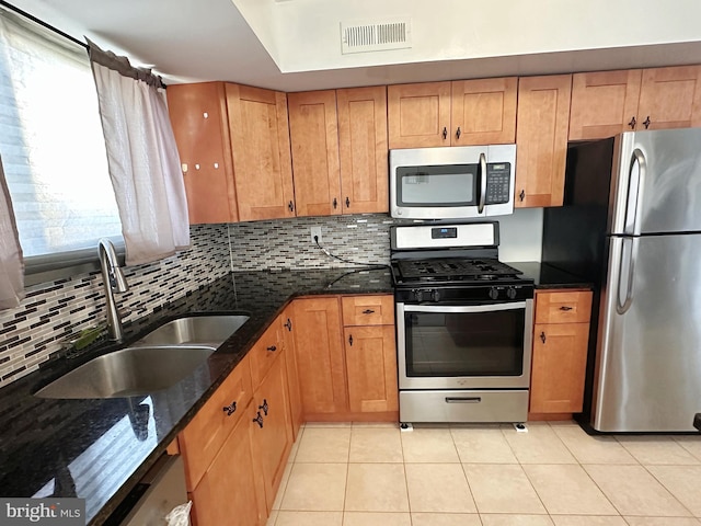 kitchen with dark stone counters, sink, decorative backsplash, light tile patterned floors, and appliances with stainless steel finishes