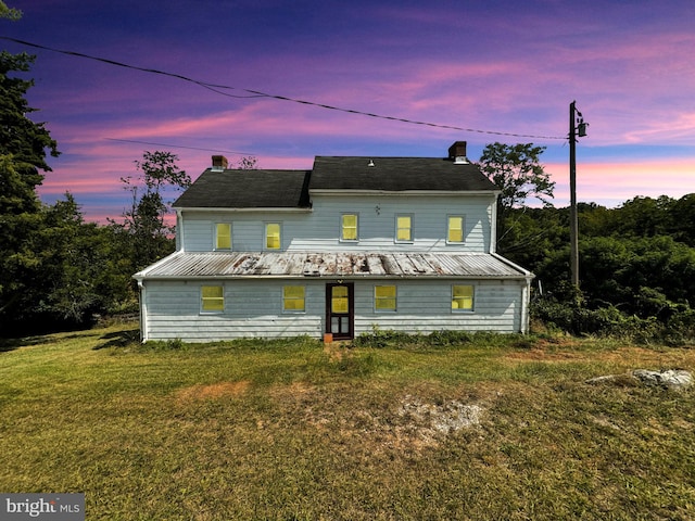 back house at dusk featuring a lawn