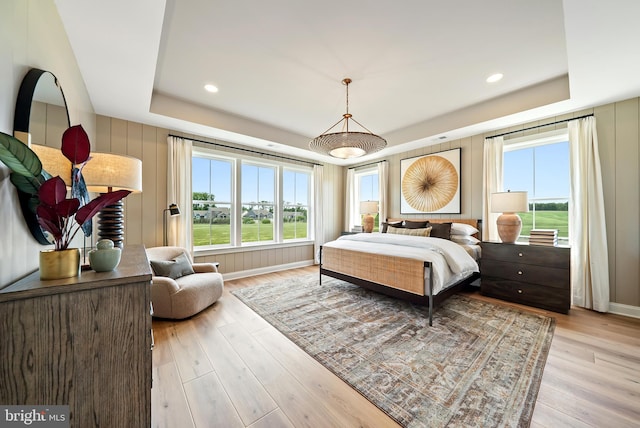 bedroom featuring multiple windows, light hardwood / wood-style floors, and a tray ceiling