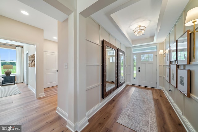 foyer entrance with a raised ceiling, an inviting chandelier, and light hardwood / wood-style flooring