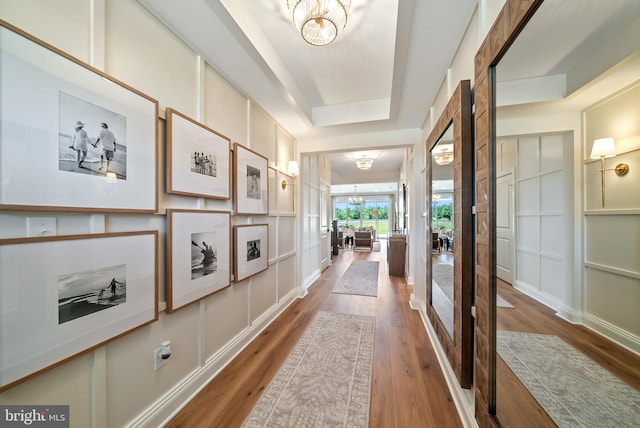 hall featuring a notable chandelier, a tray ceiling, and hardwood / wood-style flooring