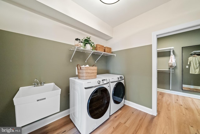 clothes washing area featuring light wood-type flooring, washer and clothes dryer, and sink