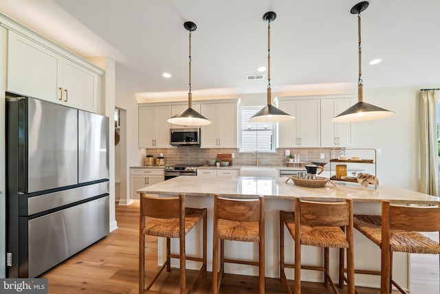 kitchen with pendant lighting, a kitchen island, stainless steel appliances, light wood-type flooring, and decorative backsplash