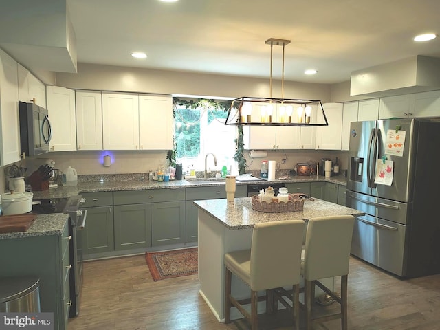 kitchen with a center island, dark hardwood / wood-style floors, appliances with stainless steel finishes, decorative light fixtures, and light stone counters