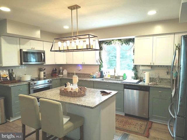 kitchen featuring stone counters, stainless steel appliances, a kitchen island, decorative light fixtures, and white cabinets