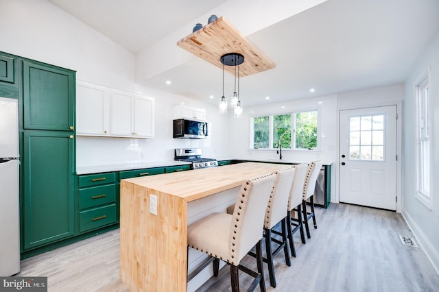 kitchen with light wood-type flooring, decorative light fixtures, stainless steel appliances, and white cabinets