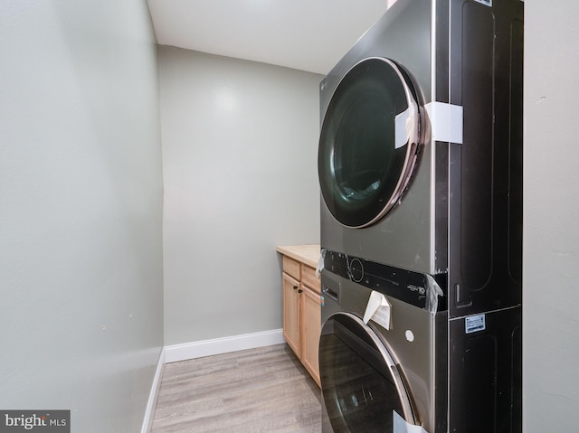 clothes washing area with light wood-type flooring, stacked washing maching and dryer, and cabinets