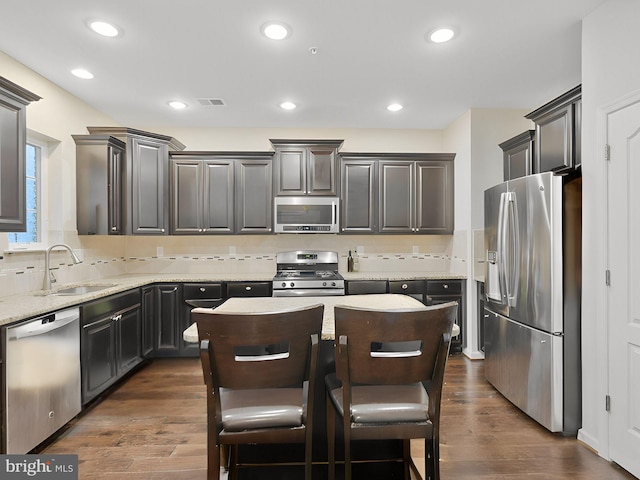 kitchen featuring sink, a kitchen island, dark wood-type flooring, appliances with stainless steel finishes, and light stone countertops