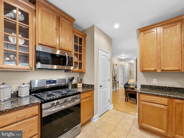 kitchen with dark stone counters, appliances with stainless steel finishes, and light tile patterned flooring