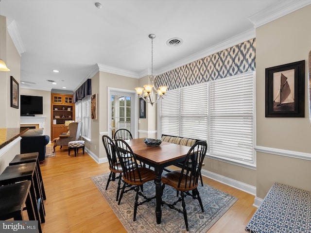 dining space featuring light wood-type flooring, ornamental molding, and an inviting chandelier