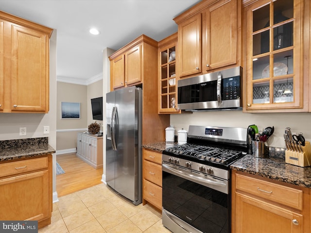 kitchen with stainless steel appliances, crown molding, light tile patterned floors, and dark stone counters