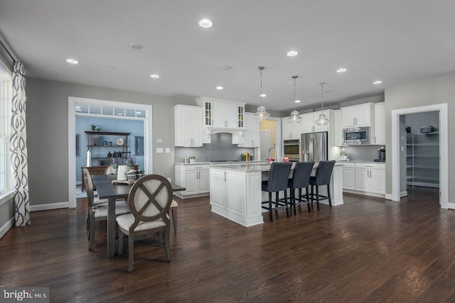 kitchen featuring hanging light fixtures, a center island with sink, dark wood-type flooring, white cabinetry, and appliances with stainless steel finishes