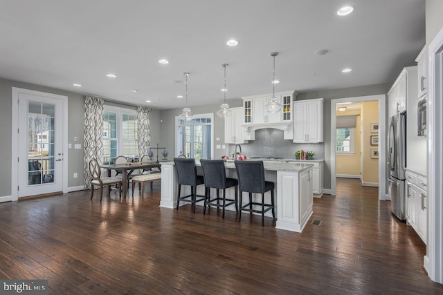 kitchen featuring a healthy amount of sunlight, white cabinets, a kitchen island with sink, and stainless steel refrigerator