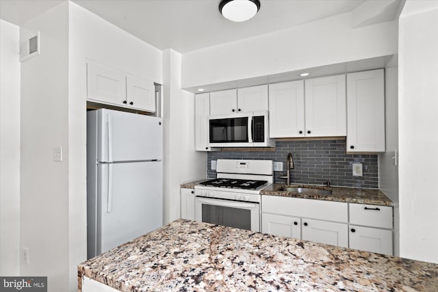 kitchen featuring white appliances, sink, light stone counters, and white cabinets