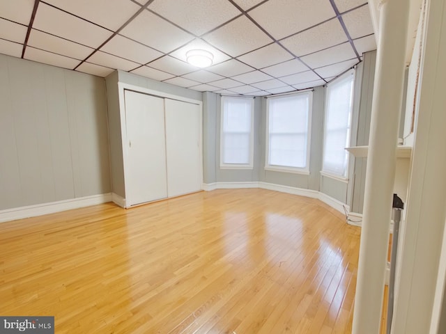 unfurnished bedroom featuring light wood-type flooring, a drop ceiling, and a closet