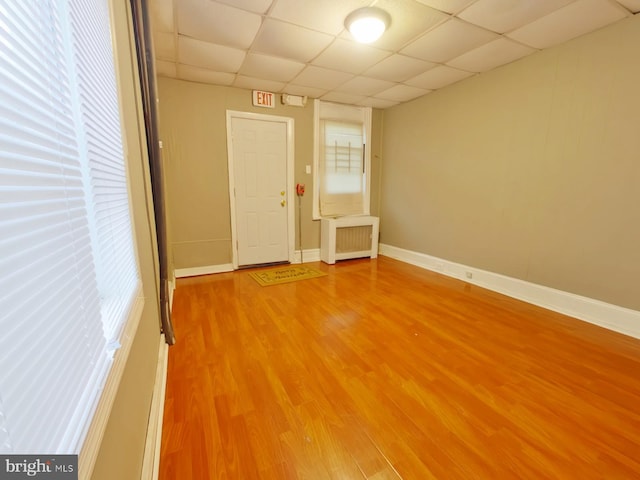 empty room with radiator heating unit, a wealth of natural light, a drop ceiling, and hardwood / wood-style floors