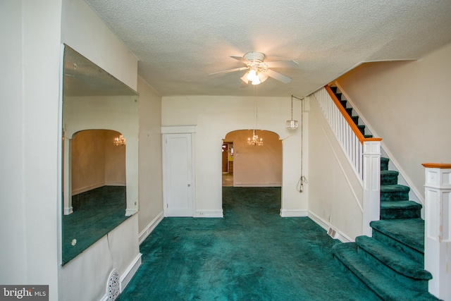 empty room with ceiling fan with notable chandelier, dark colored carpet, and a textured ceiling