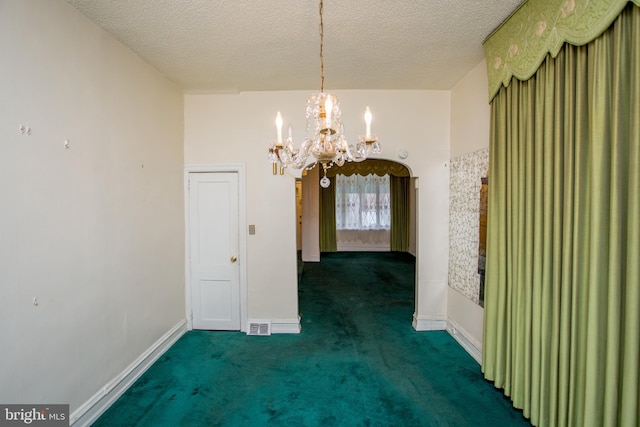 unfurnished dining area featuring an inviting chandelier, a textured ceiling, and dark colored carpet