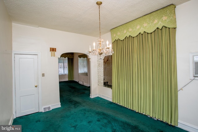 spare room featuring an inviting chandelier, a textured ceiling, and dark colored carpet