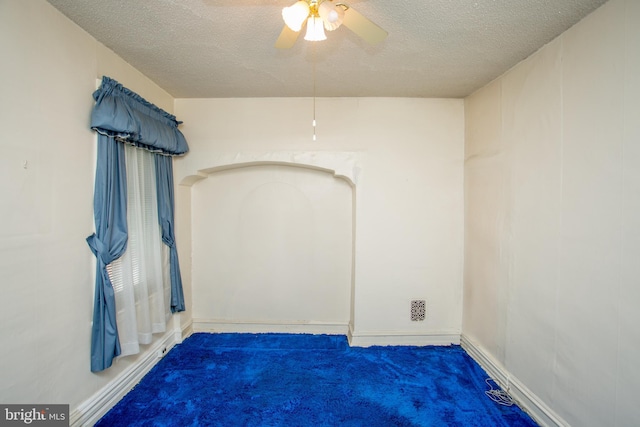 spare room with a textured ceiling, dark carpet, and ceiling fan