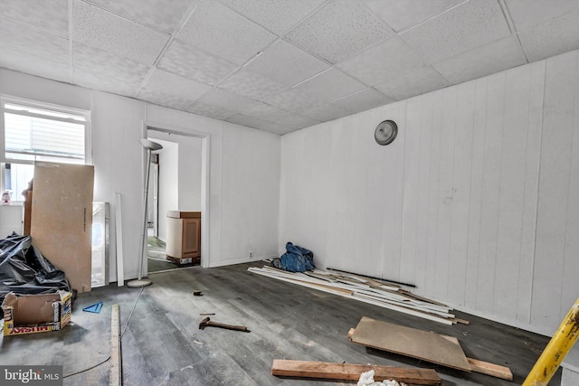 unfurnished room with a drop ceiling, wooden walls, and dark wood-type flooring