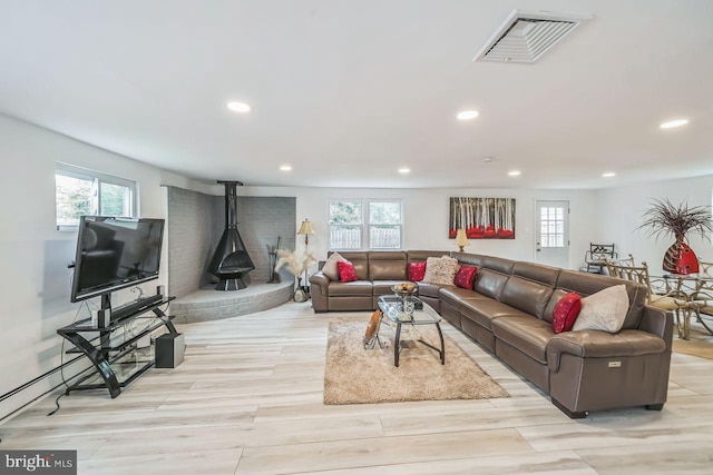 living room featuring a wood stove, a wealth of natural light, and light hardwood / wood-style flooring