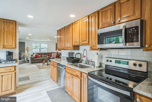 kitchen with light stone counters, sink, appliances with stainless steel finishes, light hardwood / wood-style floors, and decorative backsplash