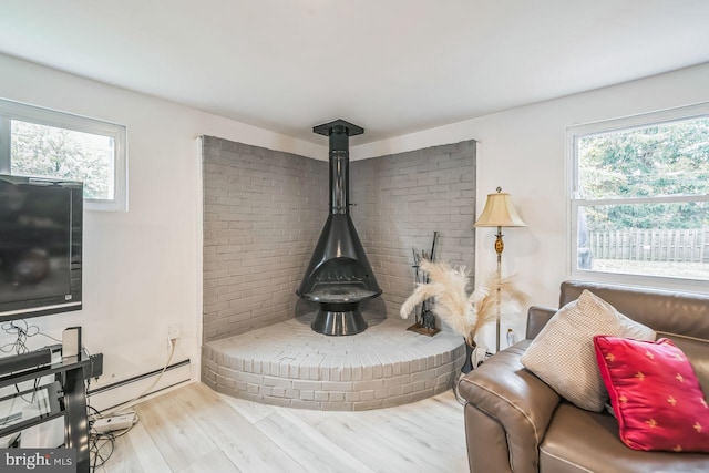 living room with light hardwood / wood-style flooring, plenty of natural light, baseboard heating, and a wood stove