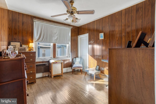 living area featuring ceiling fan, wood walls, a baseboard heating unit, and light hardwood / wood-style flooring